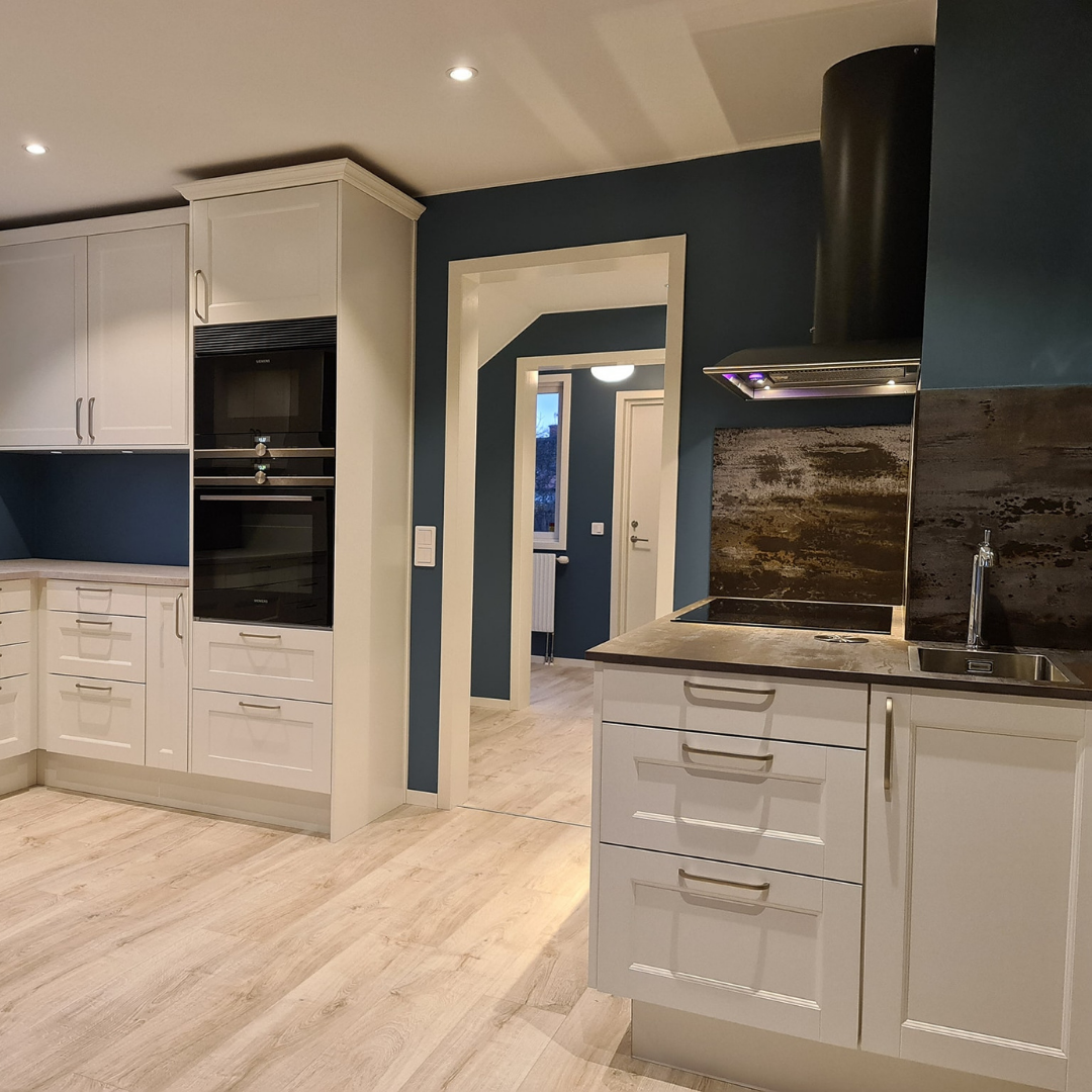 Ljust kök med vita luckor, blå väggar och kontrasterande mörk stänkskiva, en elegant köksrenovering med skandinavisk känsla.