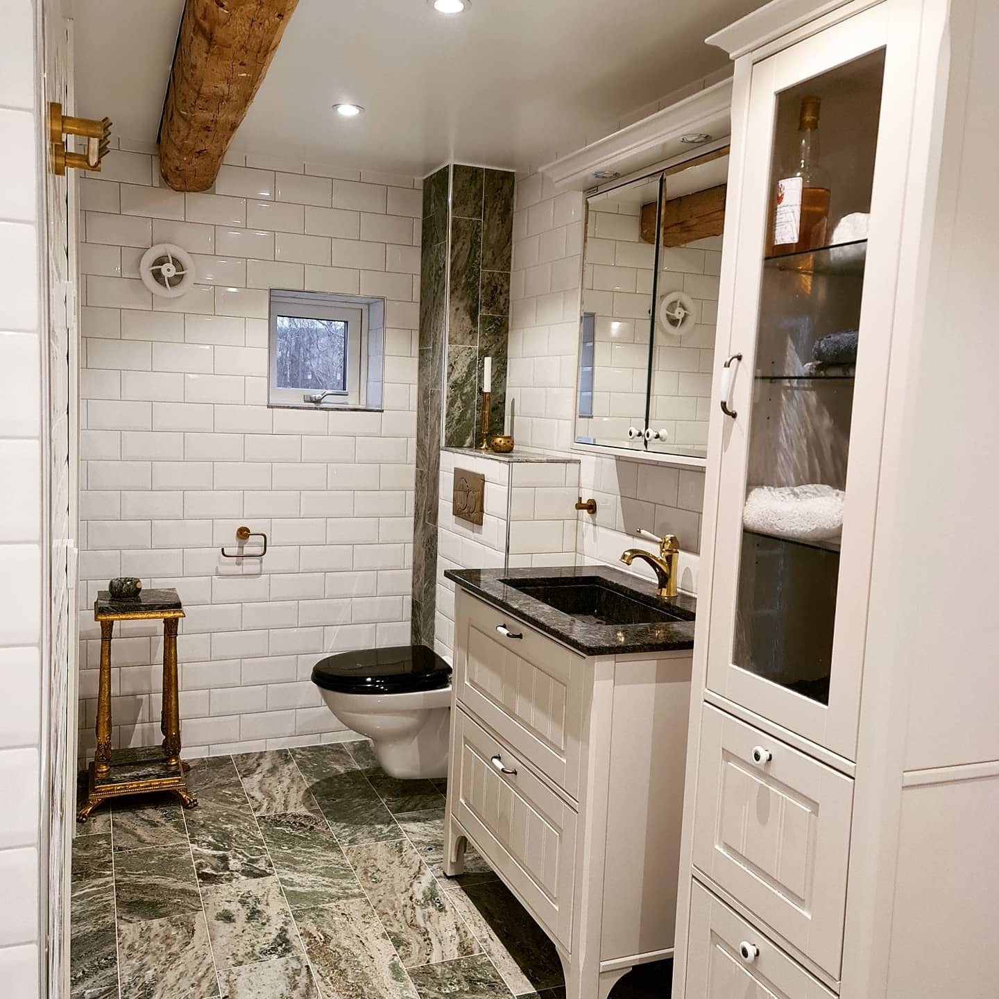 Klassiskt badrum med svart toalettlock, vitt kakel och sten/marmorgolv – badrumsrenovering i Norrköping