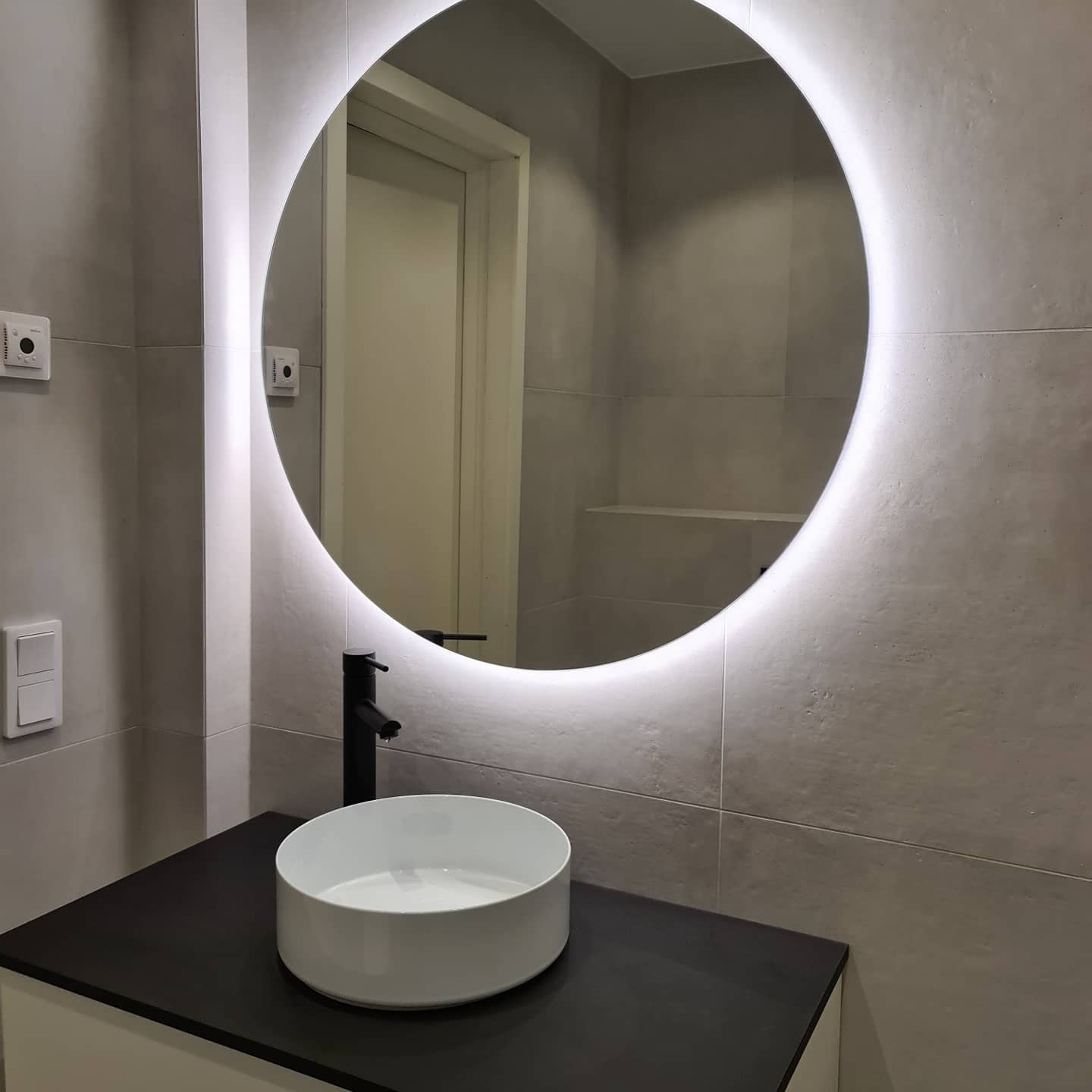 Modernt badrum med rund spegel och stilren tvättställsblandare – exempel på badrumsrenovering i Norrköping