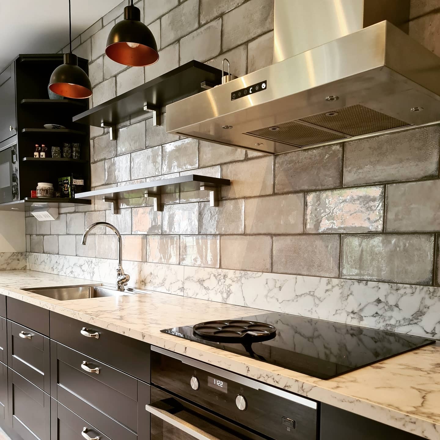 Köksrenovering med mörka luckor, bänkskiva av marmor och öppna hyllor under rostfri fläkt, snyggt och funktionellt.