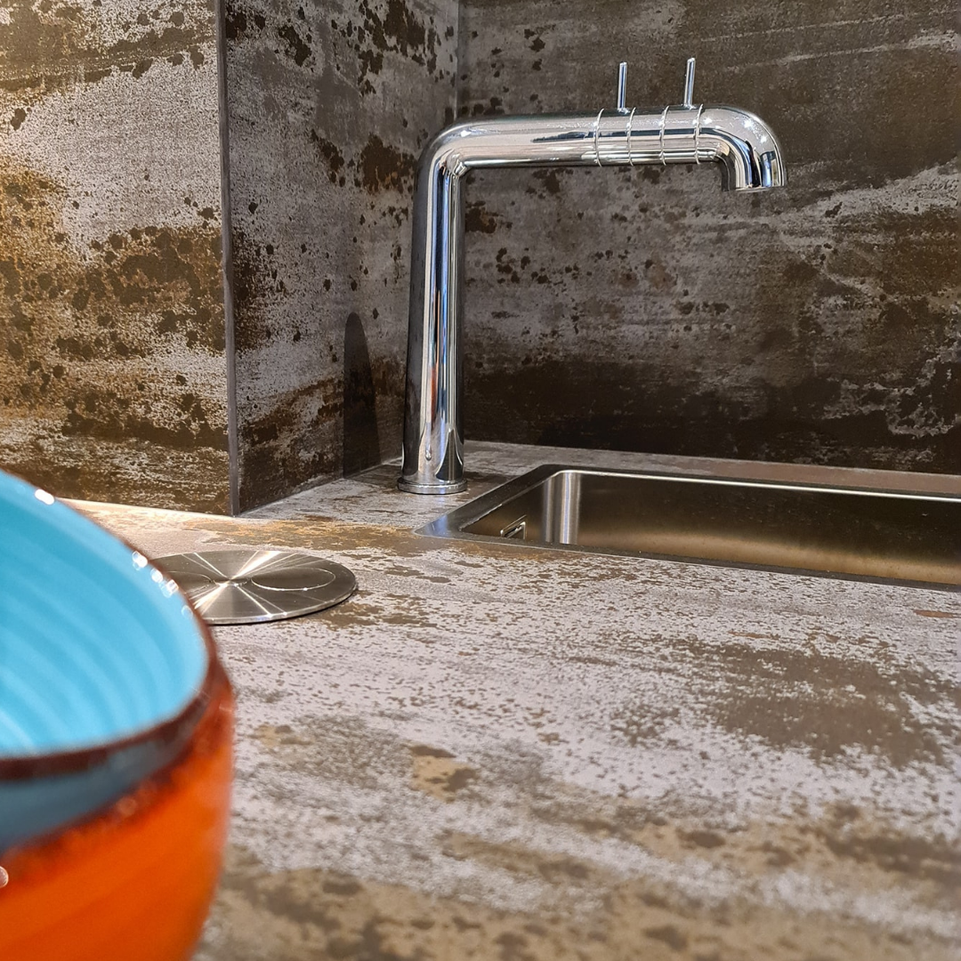 Närbild på diskho och blandare med rustik bänkskiva i stenstil, en detalj från en köksrenovering som visar på materialvalens betydelse.
