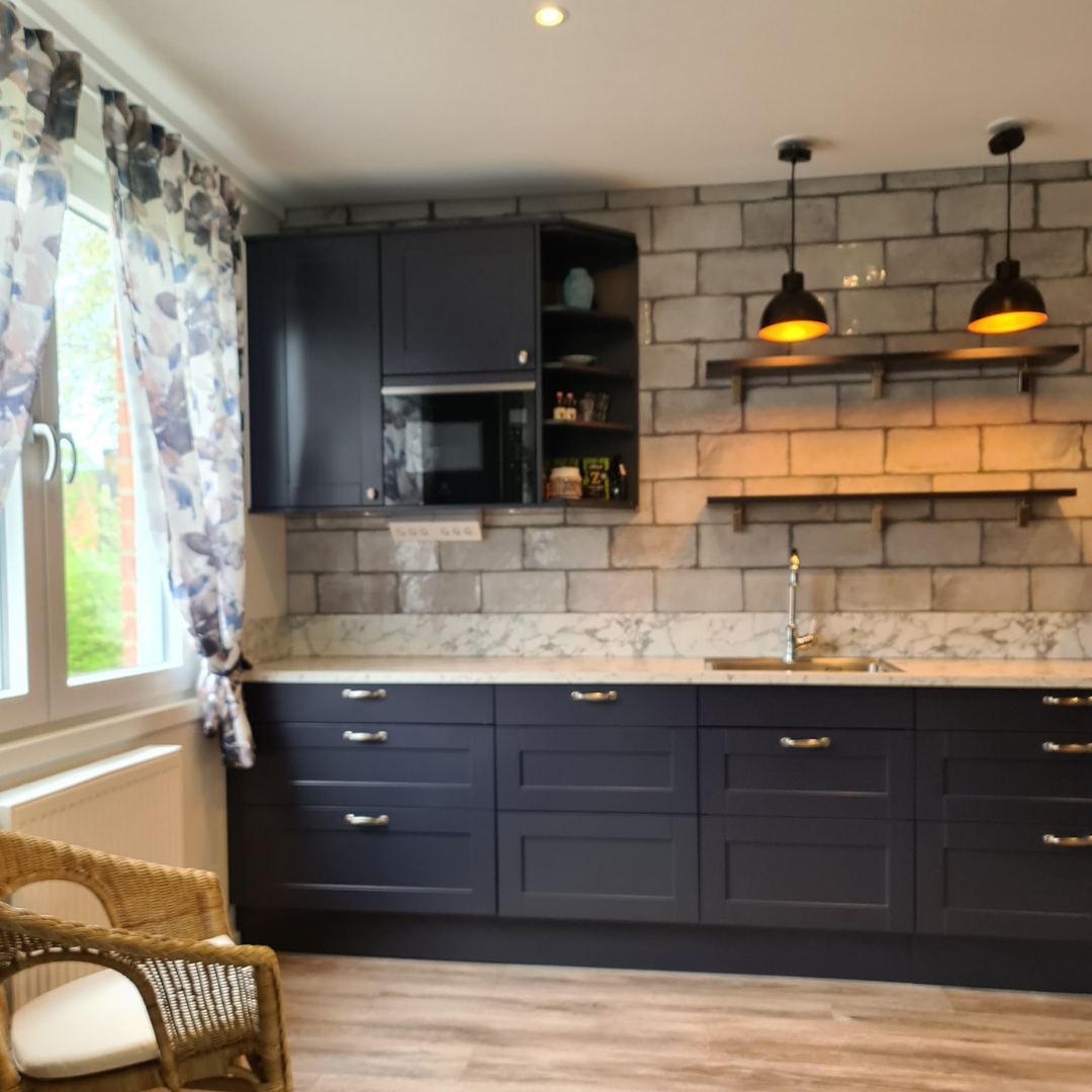Kök i mörkblå toner med stora stenskivor och öppna hyllplan, en stilfull köksrenovering som kombinerar klassiskt hantverk och modern design.