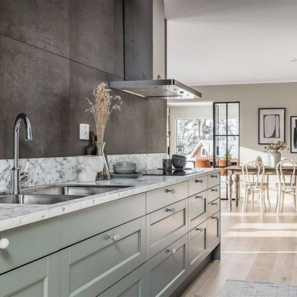Modernt kök i grågrön ton med marmorinspirerad bänkskiva och integrerad spis, ett exempel på stilren köksrenovering som kombinerar funktion med estetik.