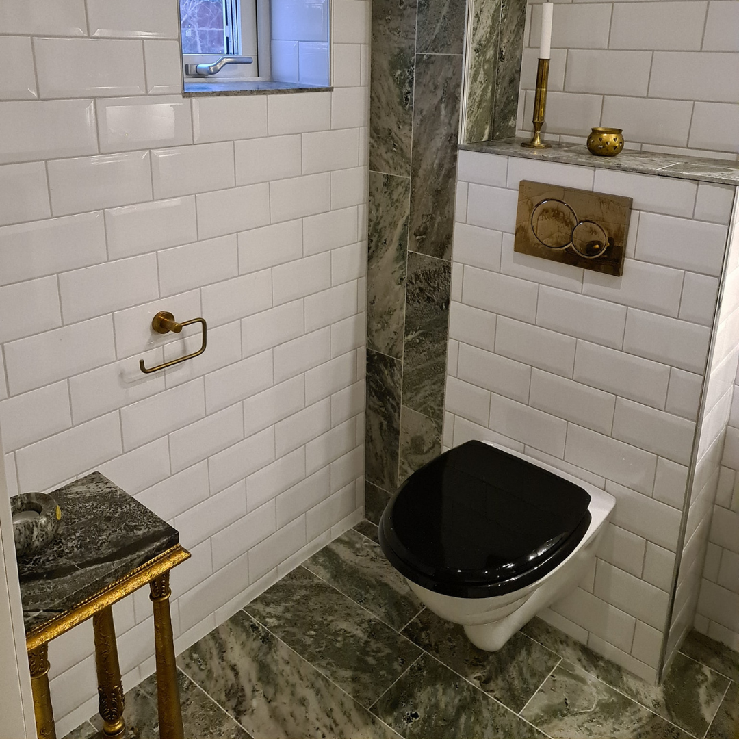 Klassiskt badrum med svart toalettlock, vitt kakel och stengolv – badrumsrenovering i Norrköping